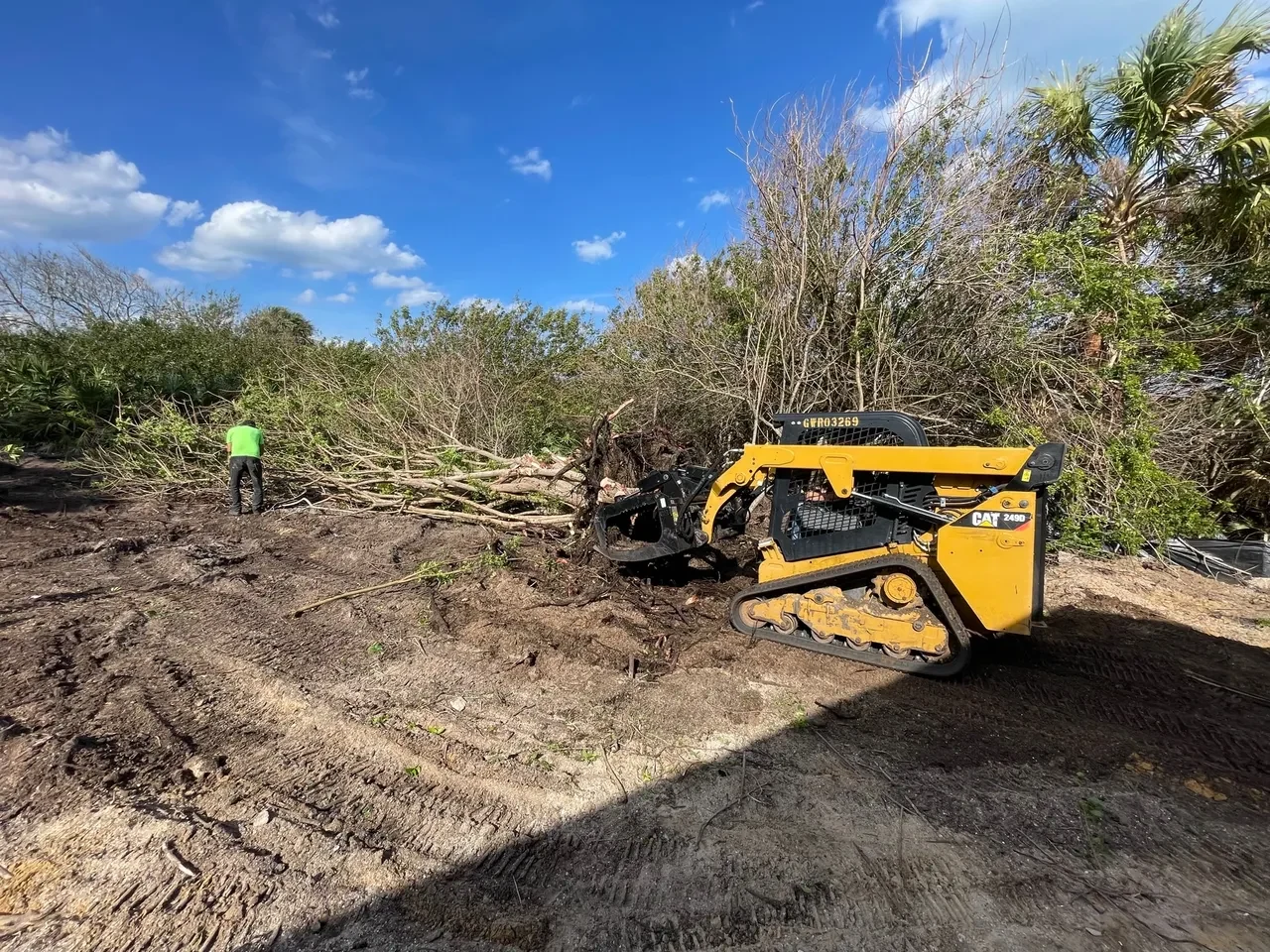 A skid steer with grapple working on brush clearing